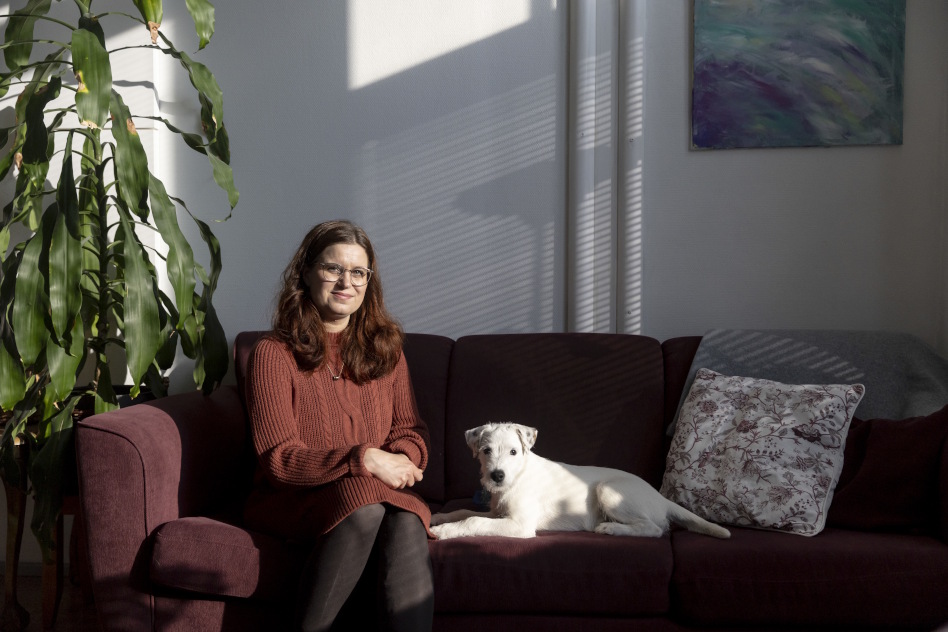 Nainen istuu sohvalla pienen, valkoisen koiran kanssa