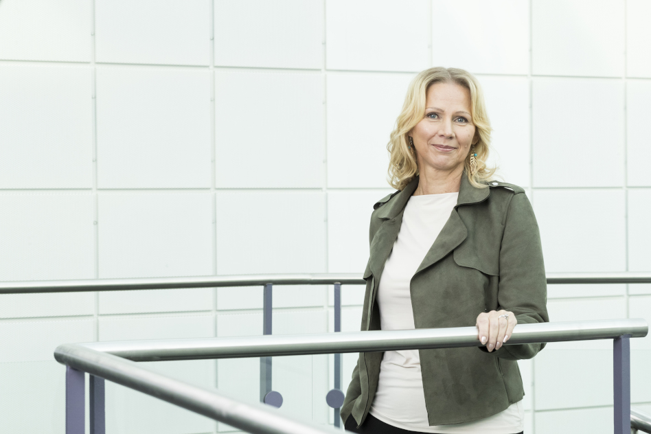 Vaaleahiuksinen nainen seisoo kaiteen edessä.