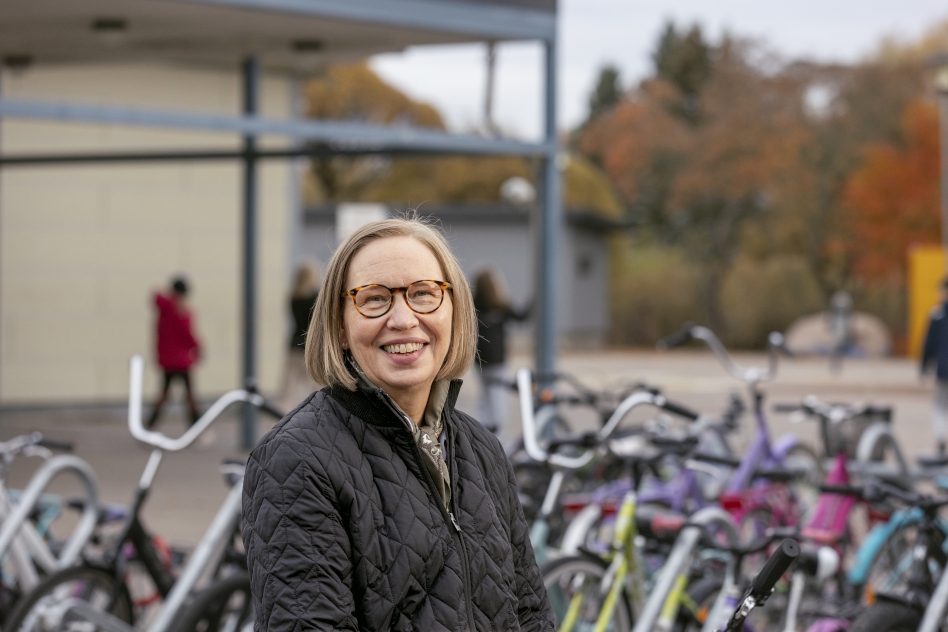 Silmälasipäinen vaaleahiuksinen nainen koulun pihalla pyörätelineen edessä