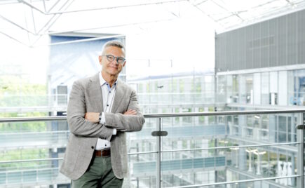 Silmälasipäinen mies seisoo kaiteen edessä kädet ristissä