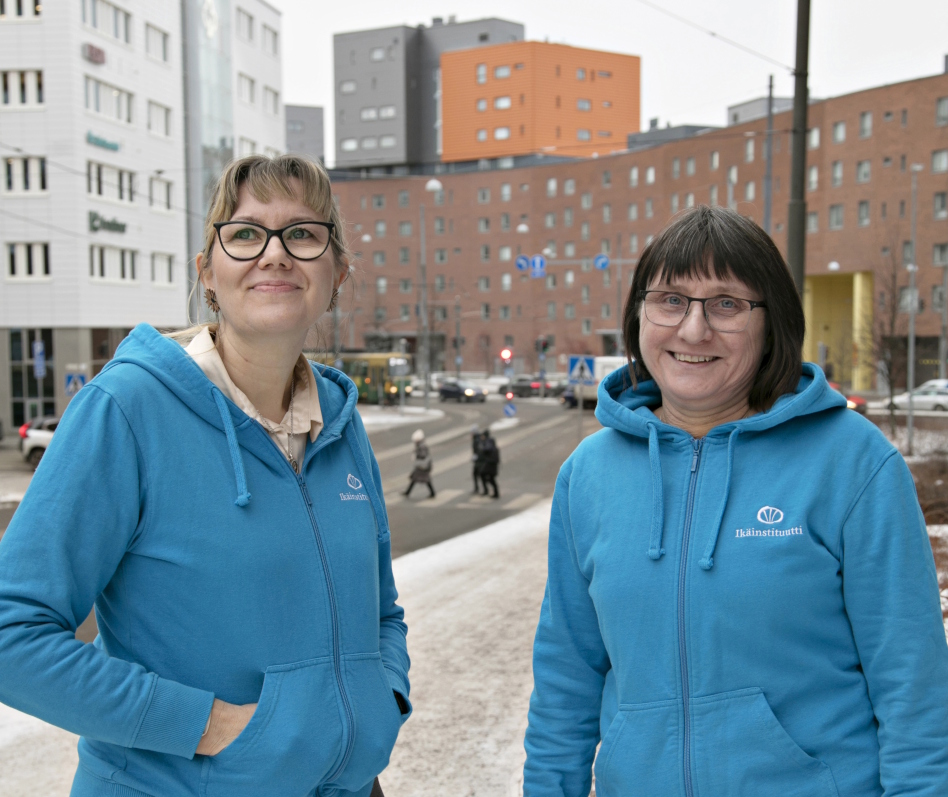 Kaksi sinisiin huppareihin pukeutunutta naista seisoo ulkona.