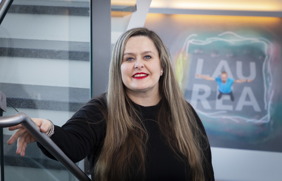 Hymyilevä nainen seinän edessä.