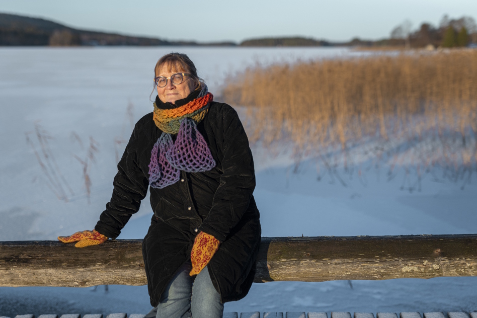 Nainen istuu puunrungon päällä järven rannassa talvimaisemassa.