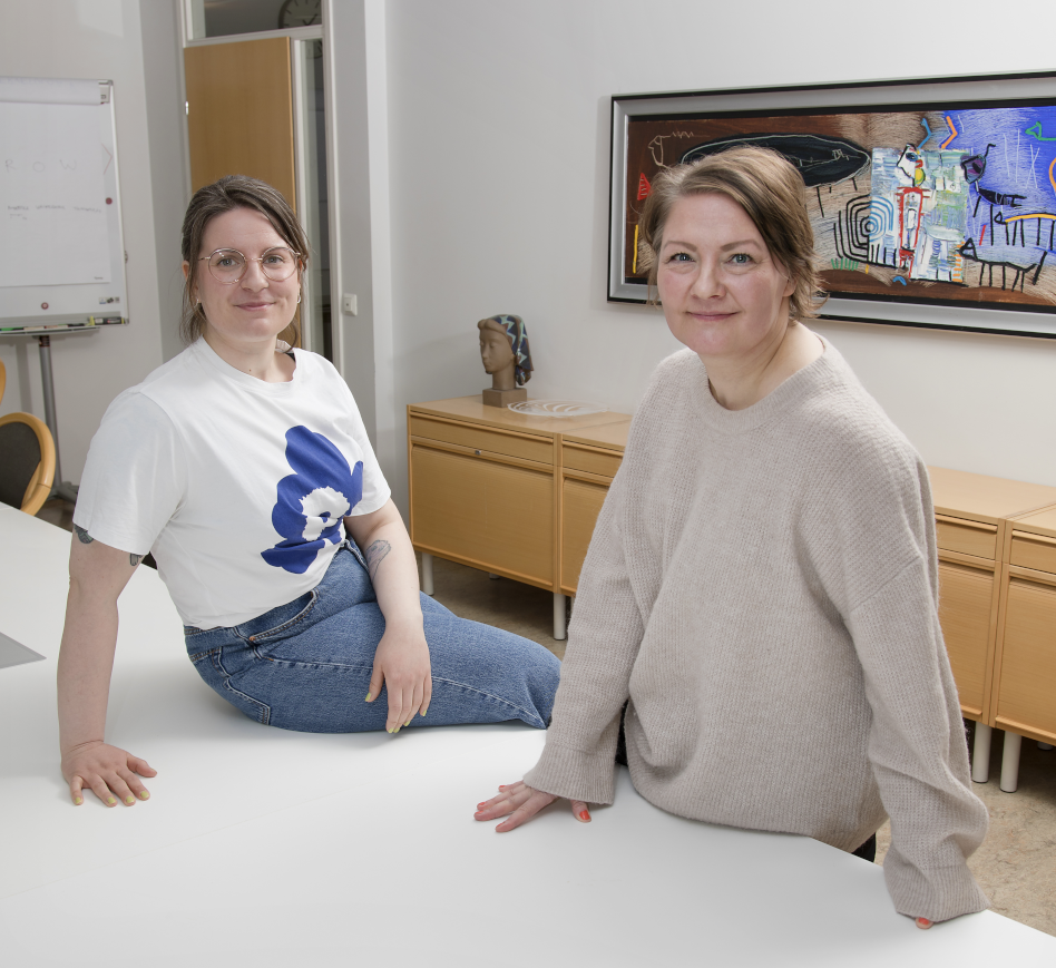 Kaksi naista nojaa työpöytään toimistolla