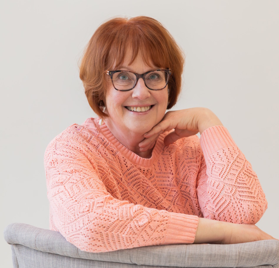 Lyhythiuksinen naine silmälasit päässä nojaa kyynärpäällä sohvaan.