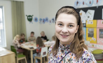 Pitkähiuksinen nainen, takana näkyy lapsia pöydän äärellä