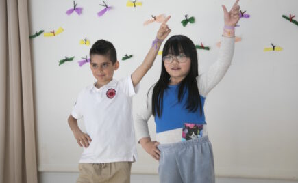 Kaksi tummahiuksista lasta seisoo toinen käsi ylhäällä