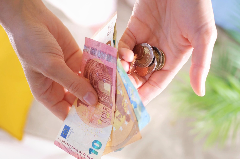 Kuva kahdesta kädestä, joissa seteleitä ja kolikoita