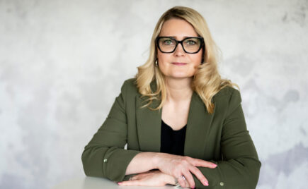 Pitkähiuksinen nainen istuu kädet ristissä vihreä paita päällä