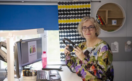 Nainen tietokoneen ääressä kuulokkeiden kanssa.