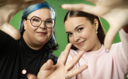 Kaksi nuorta naista vierekkäin, jotka tekevät sormilla sydämen