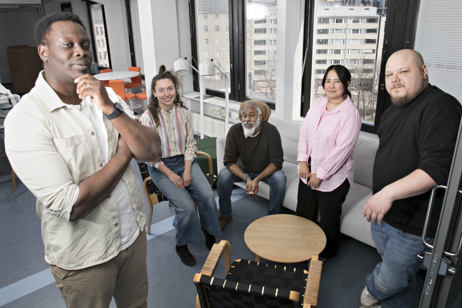 Kolme miestä ja kaksi naista istuu ja seisoo lasiseinäisessä toimistossa.