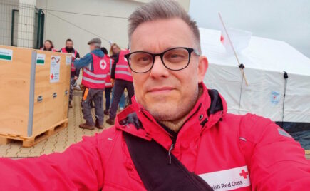 Silmälasipäinen mies punaisessa Punaisen Ristin puserossa