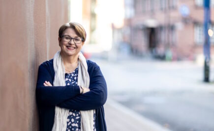 Silmälasipäinen keski-ikäinen nainen nojaa seinään kadulla