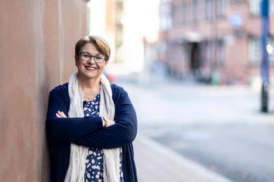 Silmälasipäinen keski-ikäinen nainen nojaa seinään kadulla