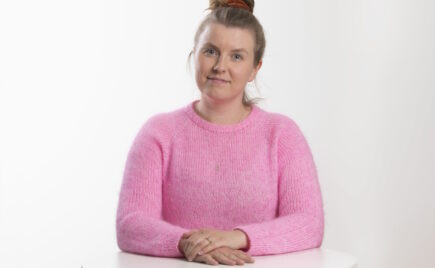 Nuori nainen pöydän ääressä vaaleanpunaisessa puserossa