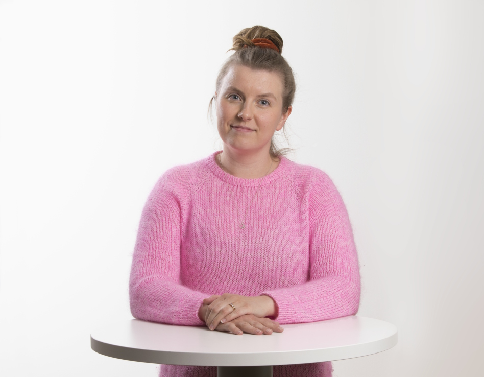 Nuori nainen pöydän ääressä vaaleanpunaisessa puserossa