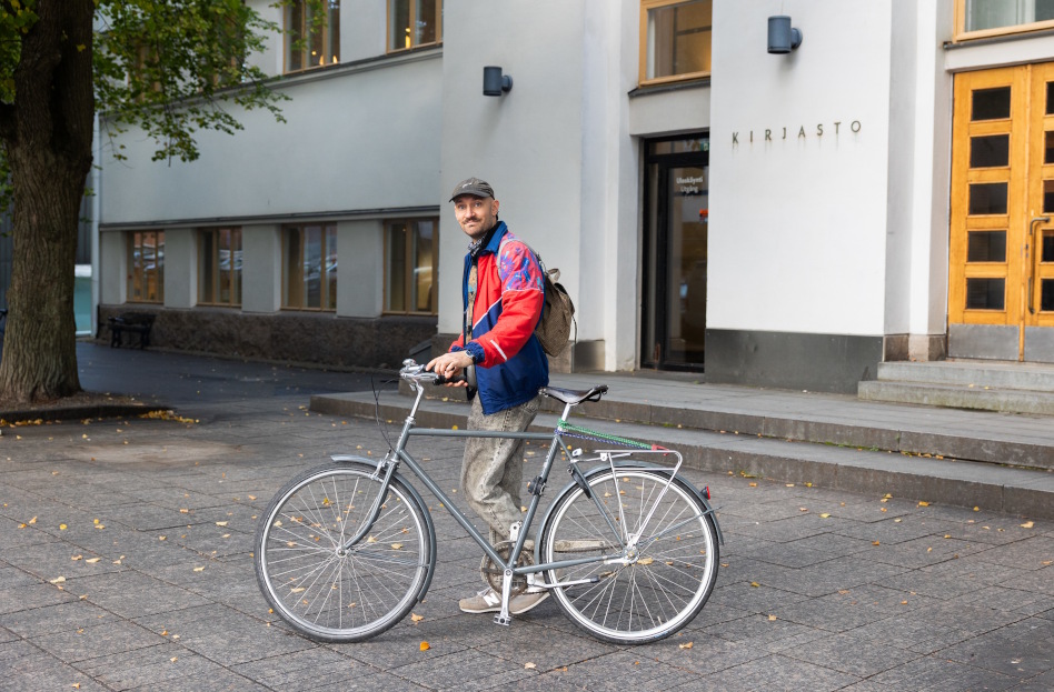 Nuori mies polkupyörän kanssa talon edessä.