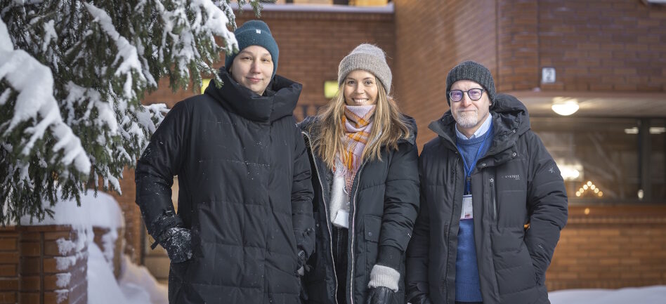 Kaksi naista ja yksi mies seisovat talvivaatteissa talon edessä