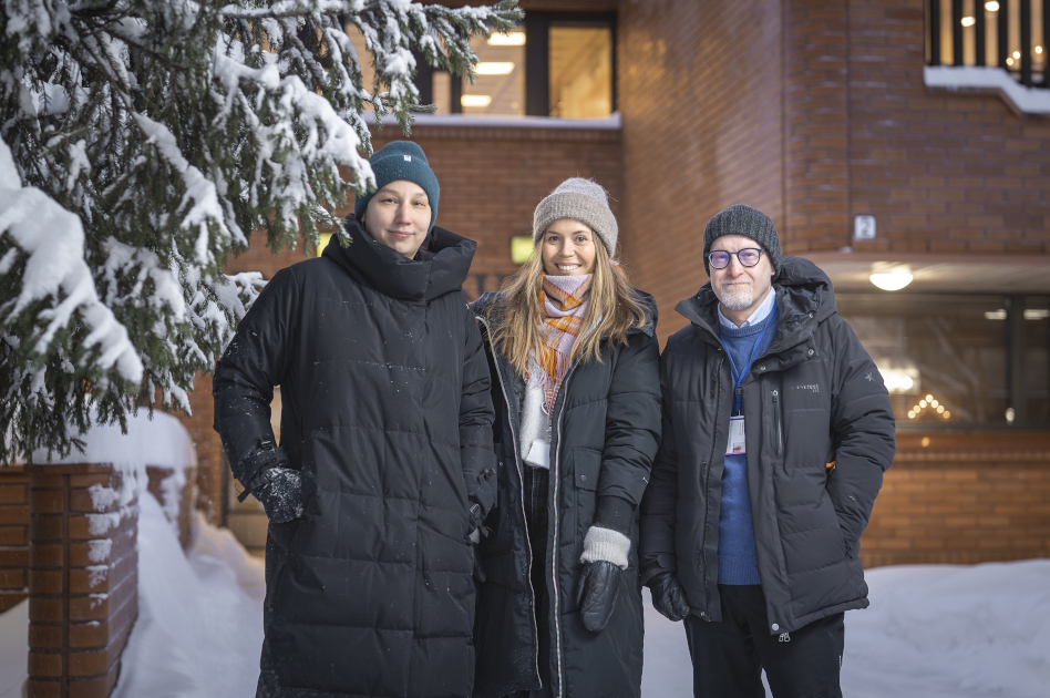 Kaksi naista ja yksi mies seisovat talvivaatteissa talon edessä