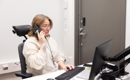 Nainen vaaleassa puserossa puhuu puhelimessa työpöydän ääressä.