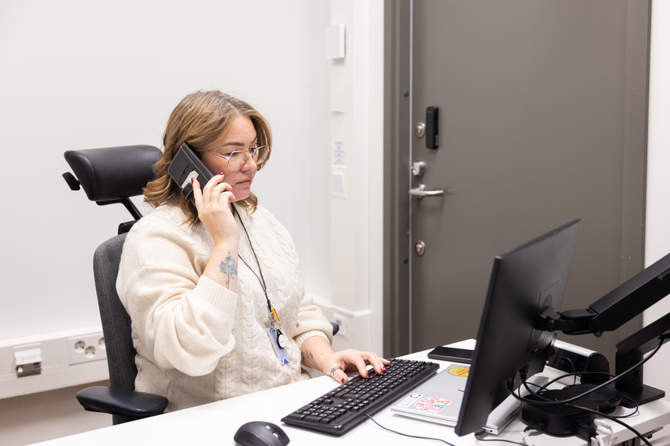 Nainen vaaleassa puserossa puhuu puhelimessa työpöydän ääressä.