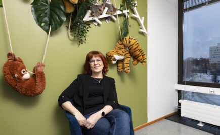 Silmälasipäinen nainen istuu seinän vieressä tuolila