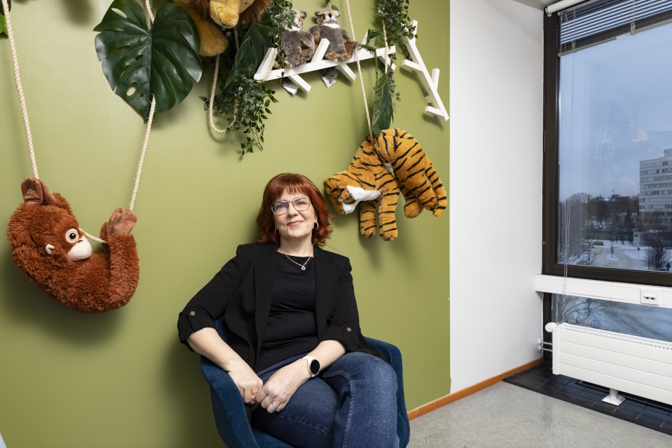 Silmälasipäinen nainen istuu seinän vieressä tuolila