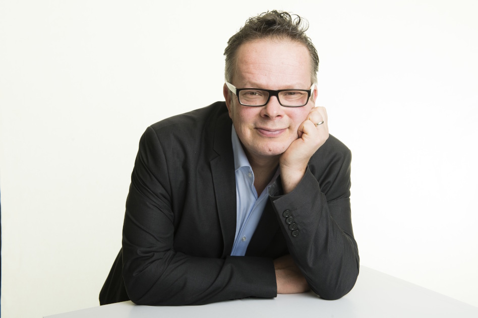 Silmälasipäinen mies puvun takki päällä nojaa pöytään