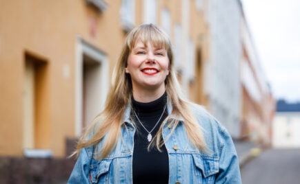 Vaaleahiuksinen nainen farkkutakissa talon edessä. Petra Malin