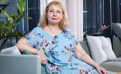 Nainen pitkässä mekossa istuu sohvalla.