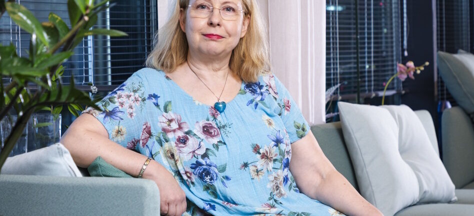 Nainen pitkässä mekossa istuu sohvalla.