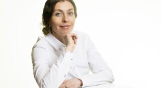 Tummahiuksinen nainen valkeassa puserossa