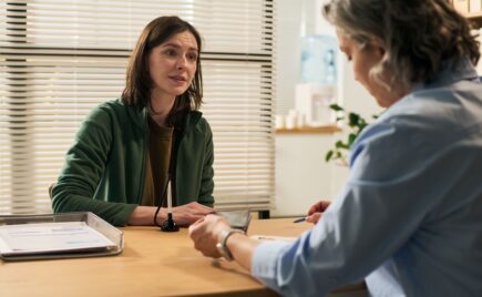 Kaksi naista keskustelee toimistomaisessa tilassa pöydän ääressä.