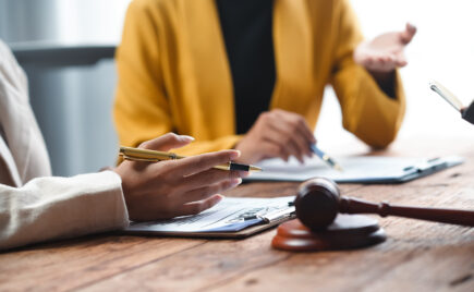 Kaksi ihmistä pöydän äärellä edessään papereita ja puheenjohtajan nuija