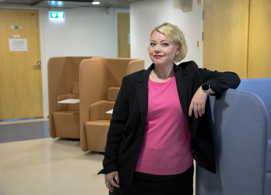 Vaaleahiuksinen nainen seisoo ja nojaa sohvaan