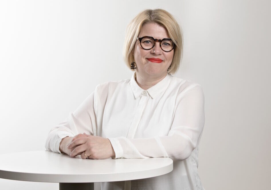Vaaleahiuksinen nainen seisoo pöydän edessä