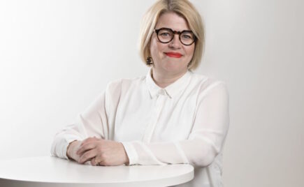 Vaaleahiuksinen nainen seisoo pöydän edessä