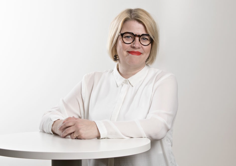 Vaaleahiuksinen nainen seisoo pöydän edessä