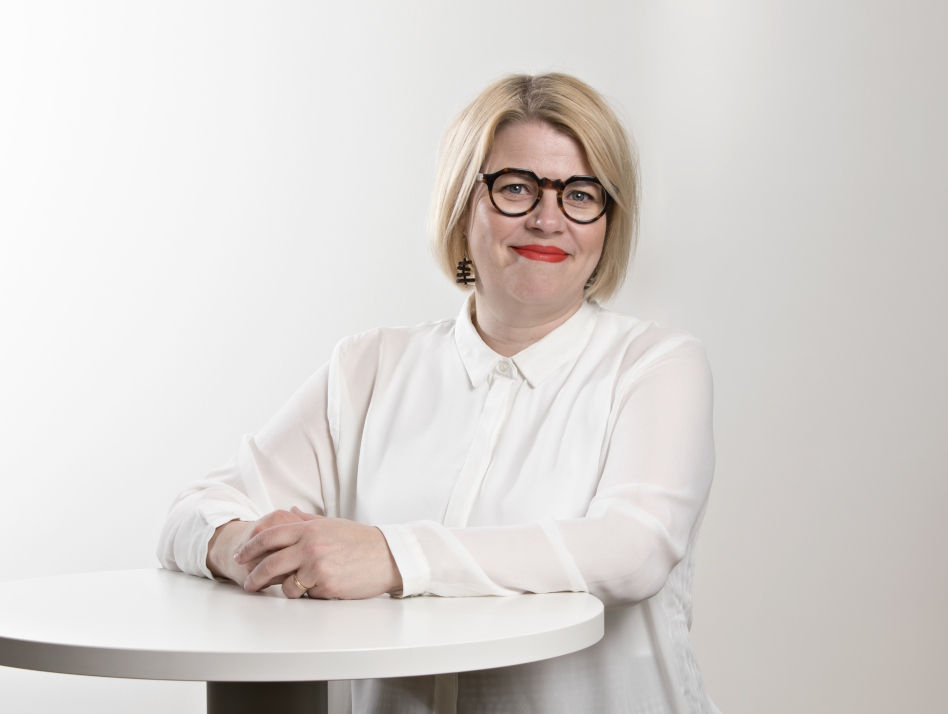 Vaaleahiuksinen nainen seisoo pöydän edessä