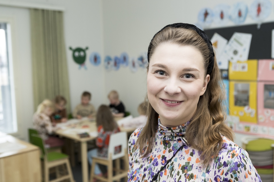 Pitkähiuksinen nainen, takana näkyy lapsia pöydän äärellä