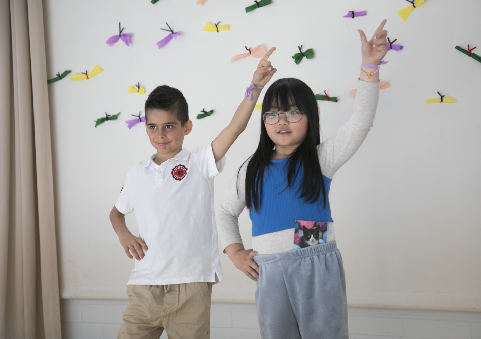 Kaksi tummahiuksista lasta seisoo toinen käsi ylhäällä