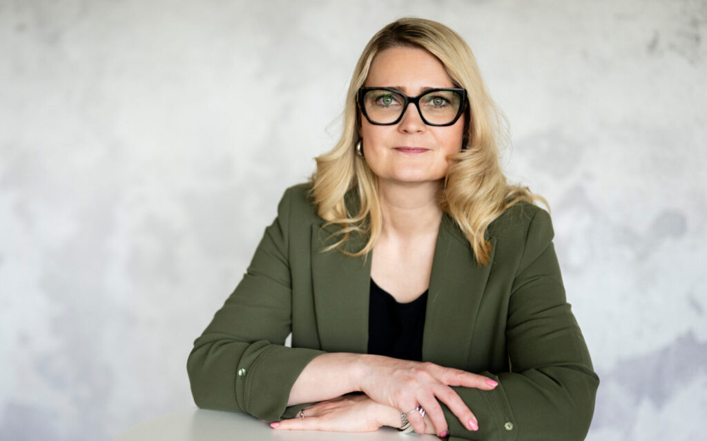 Pitkähiuksinen nainen istuu kädet ristissä vihreä paita päällä