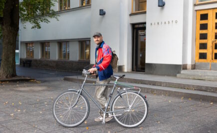 Nuori mies polkupyörän kanssa talon edessä.