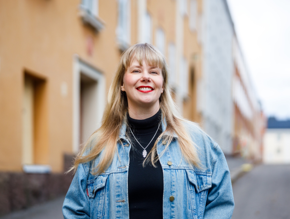 Vaaleahiuksinen nainen farkkutakissa talon edessä. Petra Malin